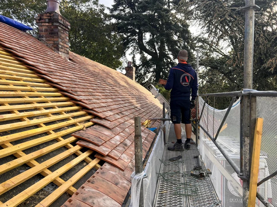 Ouvrier couvreur en tenue professionnelle travaillant sur toiture en réfection, debout sur échafaudage métallique avec garde-corps de sécurité