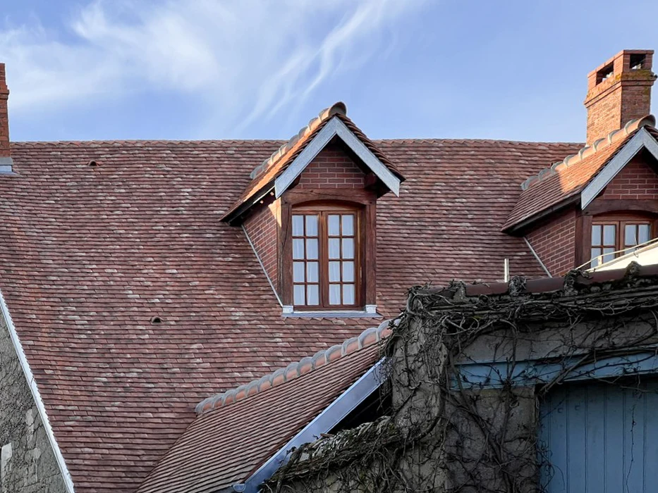 Extérieur d'une maison traditionnelle avec toiture en tuiles terre cuite et lucarnes à fenêtres à petits carreaux