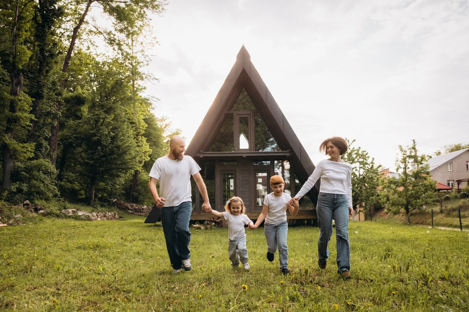 Homme d'affaires en chemise bleue protégeant de sa main des maquettes de maisons en bois disposées sur un bureau
