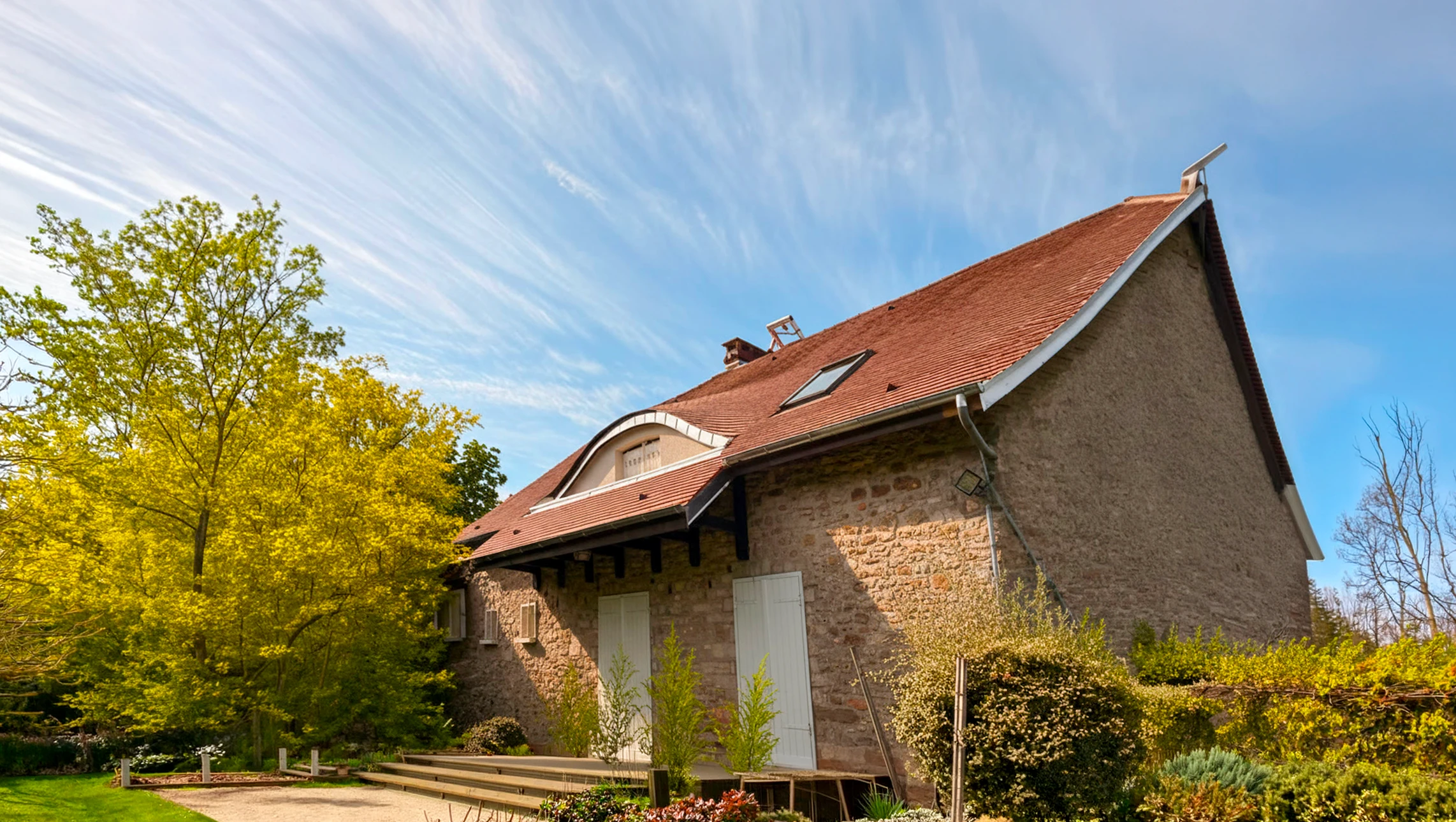 Ouvrier en combinaison bleue travaillant sur toiture en tuiles d'argile rouge-orange d'une maison méditerranéenne